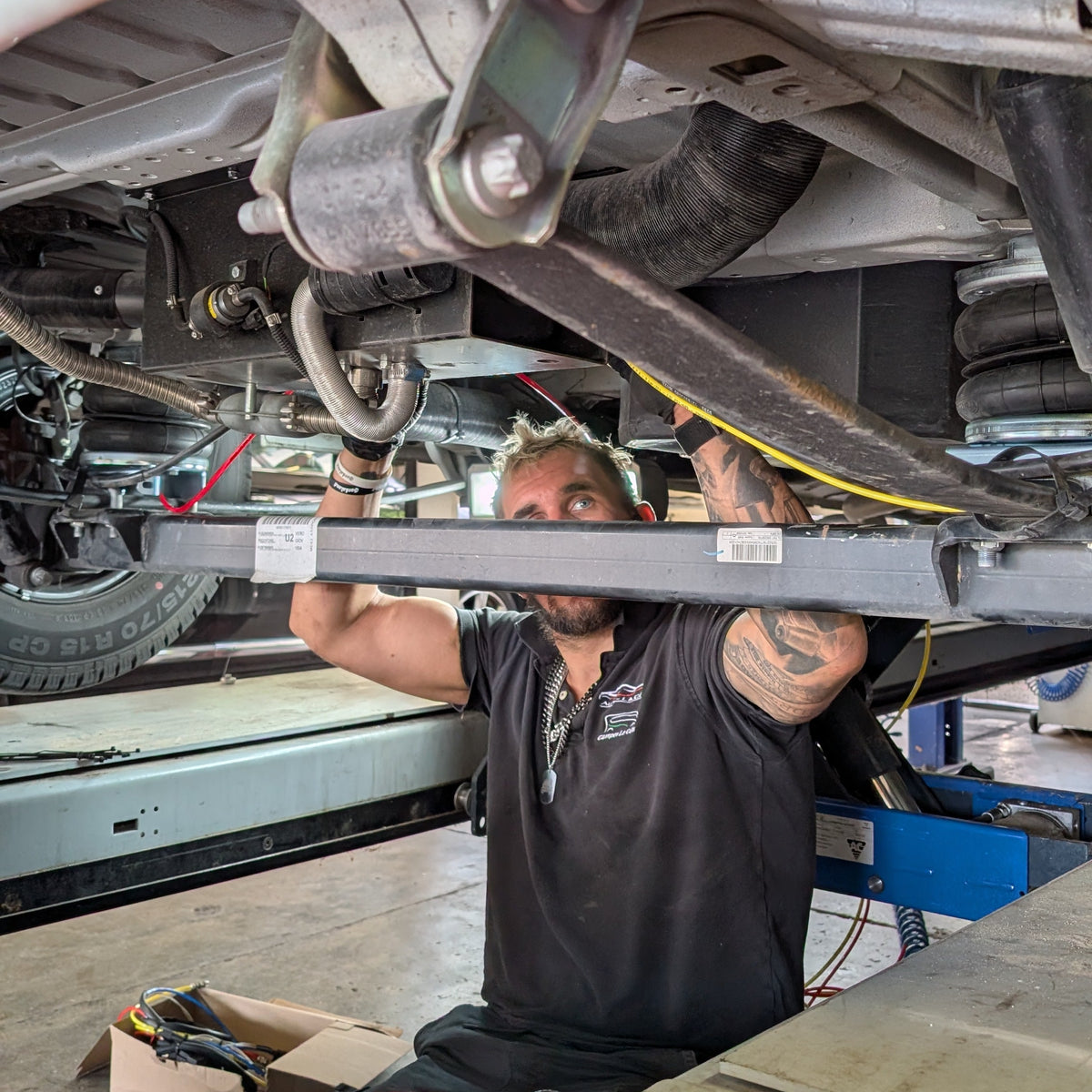 Technicien installant une suspension pneumatique sur un camping-car dans notre atelier de Begnins